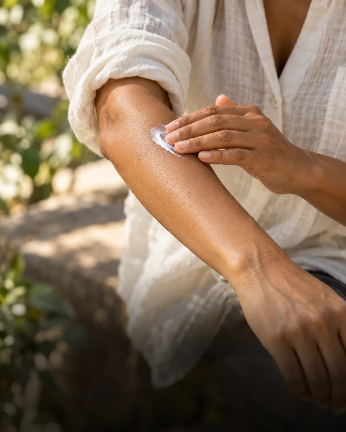 Adulte appliquant une protection solaire sur un avant-bras près d’une manche en lin, à l’ombre en extérieur